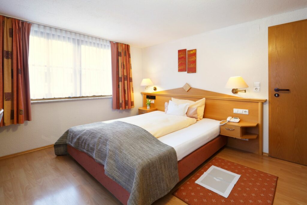 Gemütliches Einzelzimmer mit Bett, Nachttisch, Schreibtisch und großem Fenster