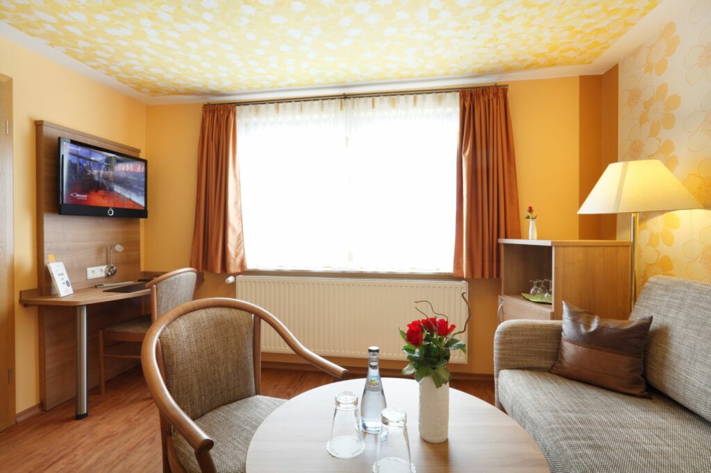 Heller Wohnbereich der Suite mit Sofa, Sessel, Tisch, TV und großem Fenster