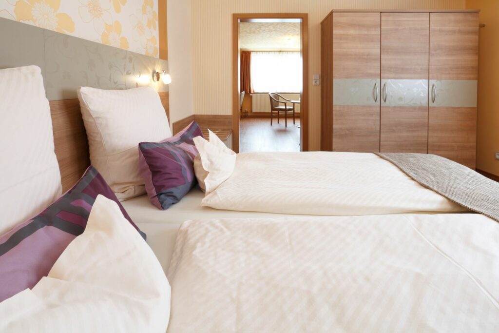 Schlafzimmer der Suite mit Doppelbett, Kissen und Blick in den Wohnbereich
